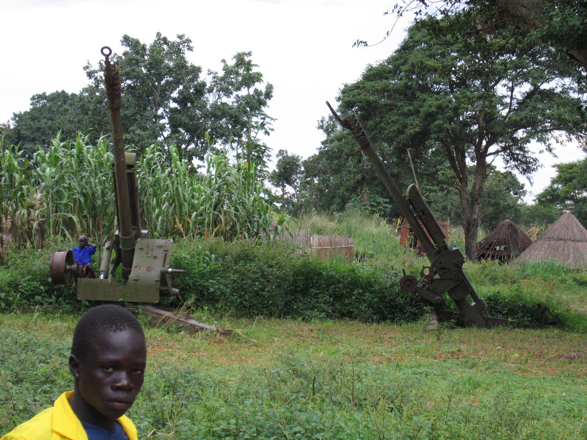 Young person passing anti-aircraft guns/light cannons in the bush of Eastern Equatoria, South Sudan