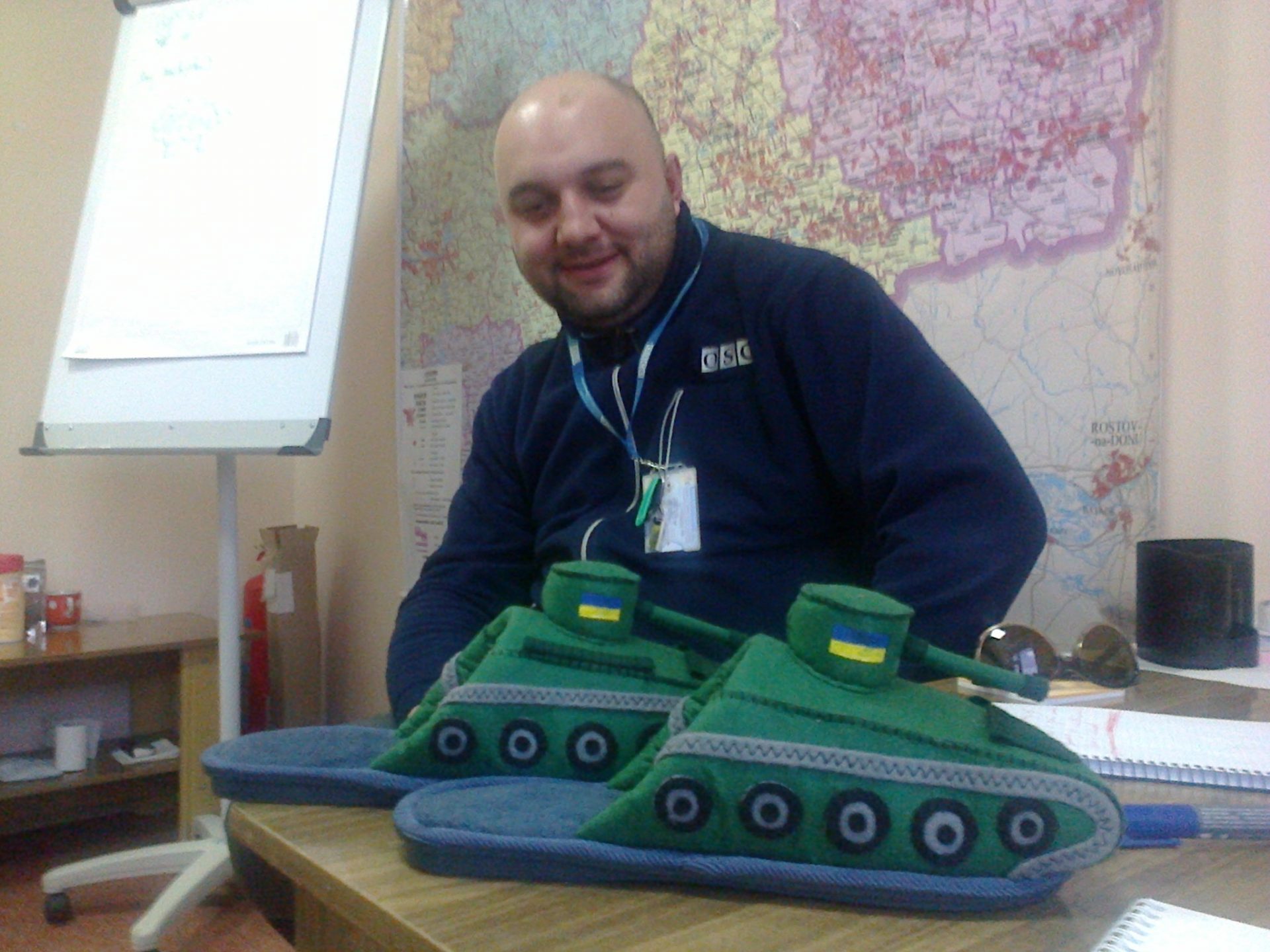 Man looks amusedly at slippers shaped as tanks.